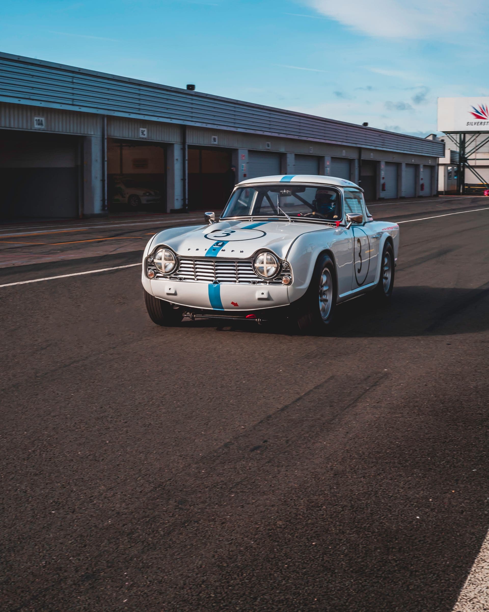 A white Triumph race car in the Silverstone pit lane